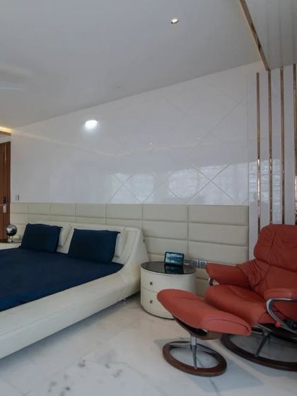 The master bedroom in the penthouse is a serene retreat, with a minimalist design, a comfortable recliner, and subtle gold accents for a touch of luxury.