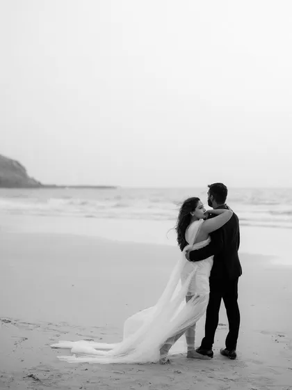 A quiet moment of connection on the vast, empty beach. The black and white tones emphasize their embrace against the backdrop of the sea, creating a timeless and classic portrait.