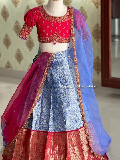 Our ethnic wear for kids is designed to be as special as yours. This half-saree for a young girl features a bright pink blouse with puff sleeves and a light blue brocade skirt, perfect for family functions.