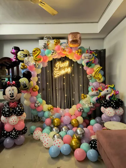 A colorful Minnie Mouse and Unicorn themed birthday party. The setup includes a circular balloon arch, character foils, and a 'Happy Birthday' neon sign.