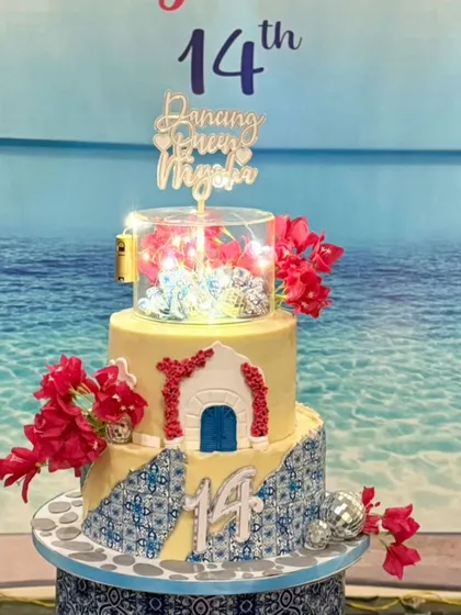 I designed this stunning Mamma Mia and Greece inspired cake for a 'Dancing Queen's' 14th birthday party. The three tiers feature iconic blue and white patterns, bougainvillea flowers, and even a tier with twinkling lights.