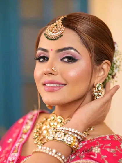A happy bride in a pink lehenga, her hands clasped, showing off her beautiful bangles and Kundan necklace.