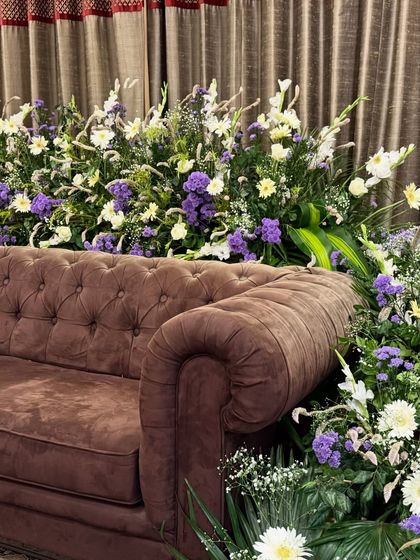 A beautiful arrangement of white, purple, and yellow flowers set against a classic brown tufted sofa. We use florals to add a pop of color and life to any space.