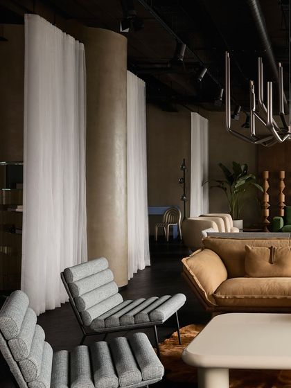 A detail shot showing the texture of the grey ribbed armchairs and the soft fabric of the sofa. The sheer white curtains act as a soft divider between different zones.