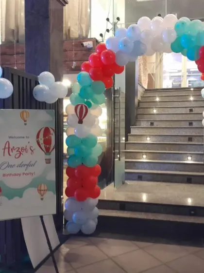 A whimsical hot air balloon themed entrance, featuring a custom welcome sign and a colorful balloon arch to greet guests as they arrive for Arzoi's first birthday party.