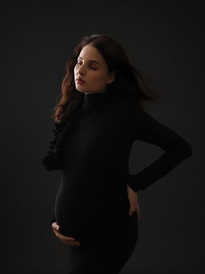 A contemplative and moody portrait. The dark background and simple black dress create a dramatic and intimate image that focuses on the mom-to-be's inner world.