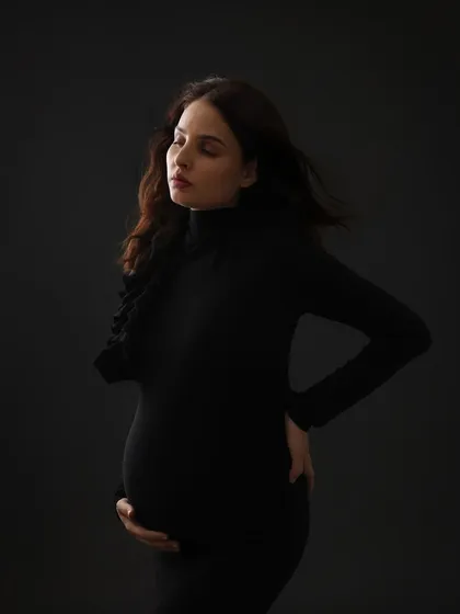 A contemplative and moody portrait. The dark background and simple black dress create a dramatic and intimate image that focuses on the mom-to-be's inner world.