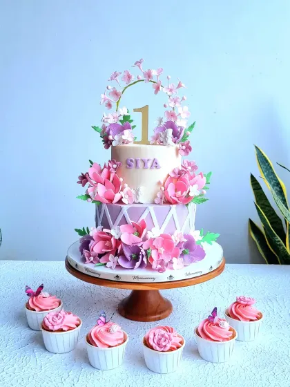 A beautiful two-tiered first birthday cake with a garden theme. It features a cascade of handmade pink and purple sugar flowers and a delicate floral hoop topper.