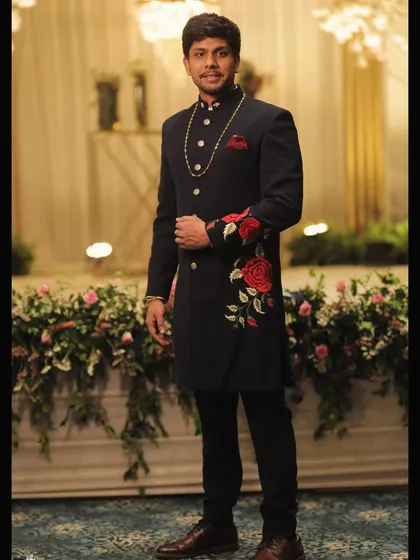 We blend tradition with modern artistry. This bespoke navy sherwani features intricate red rose embroidery, creating a standout piece for any grand occasion. Our expertise in traditional Indian menswear ensures you look regal and unique.