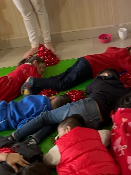 After a fun game, the children lie down for a moment of rest, still surrounded by festive red pom-poms.