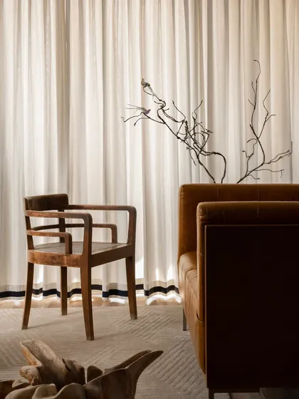The story of a space is often told in its details. Here, a handcrafted wooden chair with a cane seat brings a sense of tradition, creating a beautiful dialogue with the rich texture of a camel-toned leather sofa. It is a pairing rooted in contrast yet tied together by an earthy, timeless tone.