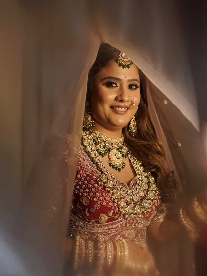 A dreamy shot of the bride under her veil. The soft focus highlights her glowing makeup and the intricate details of her green-beaded jewellery.