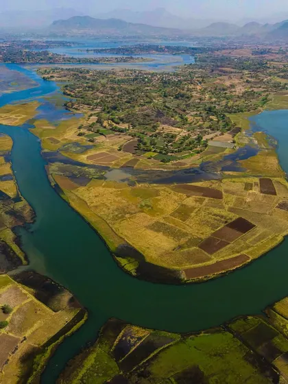 The river bends around farmland near the Mumbai-Agra Highway. This aerial shot shows the beautiful contrast between man-made infrastructure and the natural flow of the land.