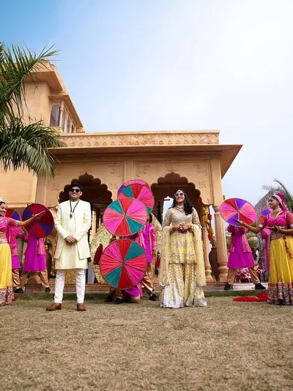 The couple posing with their entourage of dancers holding colorful umbrellas, perfectly capturing the festive Rajasthani theme.