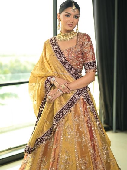 A full view of this stunning traditional bride. The makeup is perfectly balanced to complement the vibrant colors and heavy embroidery of her lehenga.