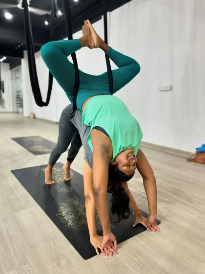 The smiles say it all. This partner pose is all about fun, support, and seeing things from a new perspective. One partner enjoys an assisted inversion while the other provides a stable base in a forward bend.