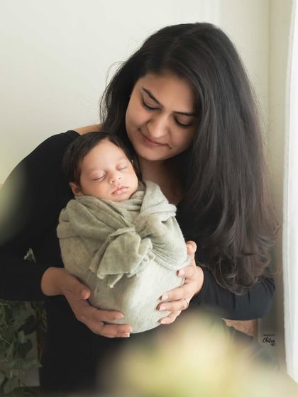 A mother's quiet moment with her sleeping baby. The soft focus on the foreground elements draws all the attention to her gentle expression and the peaceful infant in her arms.