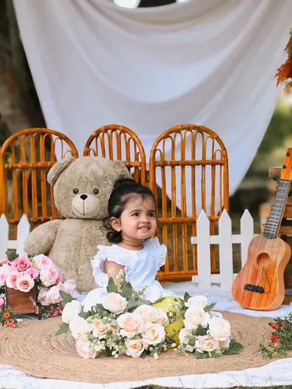 A beautiful outdoor portrait for a first birthday. The rustic setup includes a teddy bear, a mini guitar, and wooden 'ONE' blocks, all set against a lovely natural backdrop.