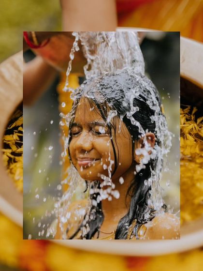 An artistic shot of a young woman during her Mangala Snaanam, capturing the moment water splashes over her.