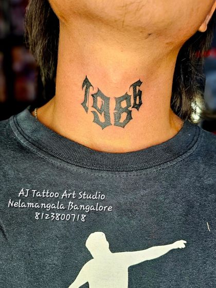 A bold "1986" birth year tattoo in a gothic font on the neck.