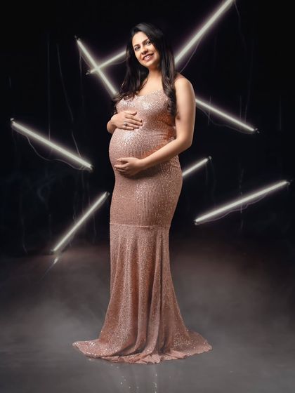 A confident and smiling portrait of a mom-to-be, looking radiant in a sequin gown and modern studio lighting.