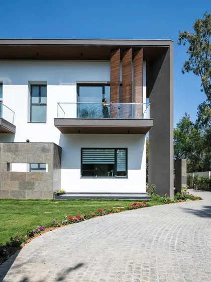 The front facade of Triveni Farmhouse, showing how vertical wooden louvers provide privacy for the balcony while adding a textural element that contrasts with the smooth white walls.