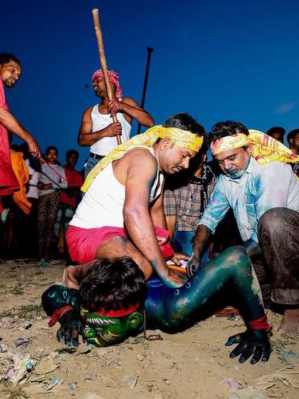The raw, physical energy of the Gajan festival in Bengal is on full display as performers engage in ritualistic struggles on the ground.