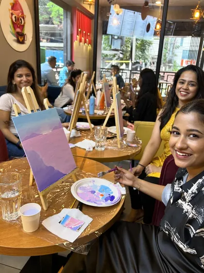 Three friends smiling and painting at a cafe, enjoying a creative and social afternoon.