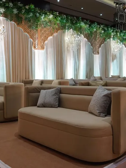 A luxurious lounge area with comfortable beige sofas, set against a backdrop of elegant drapes and chandeliers, providing a stylish space for guests to relax.