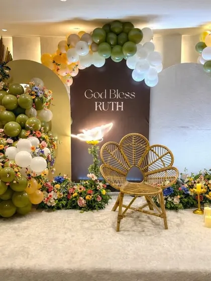 An elegant and modern blessing ceremony for baby Ruth. We combined an earthy palette of olive green and white balloons with lush floral arrangements, a stylish wicker peacock chair, and warm candlelight to create this serene and beautiful stage.