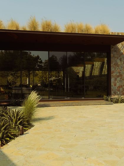A closer view of the pavilion entrance, showing the blend of stone, glass, and the wild grass roof.