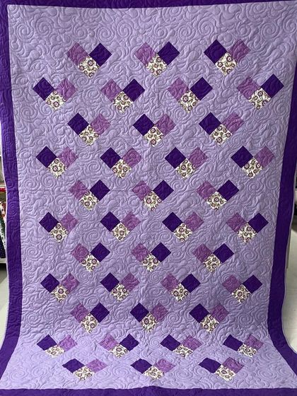 A simple but elegant quilt with a repeating block pattern in shades of purple.