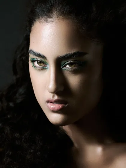 An intense beauty close-up with a focus on the dramatic green eye makeup. The lighting is soft but directional, emphasizing the model's strong features.