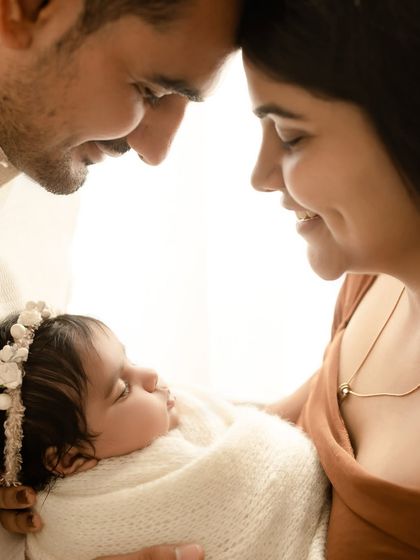 An intimate close-up of parents and their newborn. Their faces frame the sleeping baby, creating a circle of love and warmth.