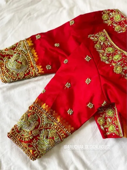 An embellished red blouse with heavy zardosi work on the sleeves, featuring traditional peacock motifs.
