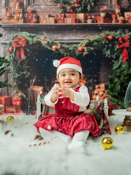 A happy baby girl in a red velvet dress, clapping her hands with delight in the Christmas set.