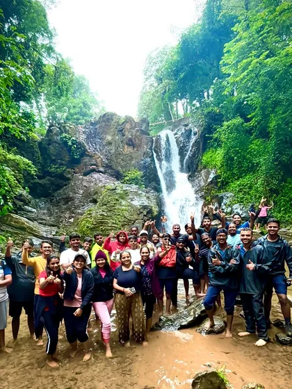 A large, happy group giving thumbs-ups while enjoying a dip in a waterfall on the Bandaje trek.