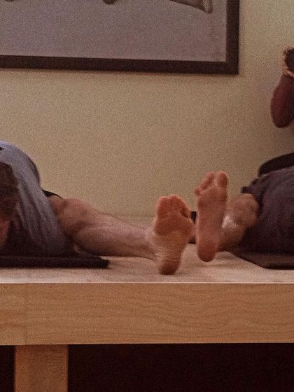 A close-up of practitioners in Kurmasana (Tortoise Pose), a deep hip-opening and forward-bending asana that requires immense flexibility and focus.
