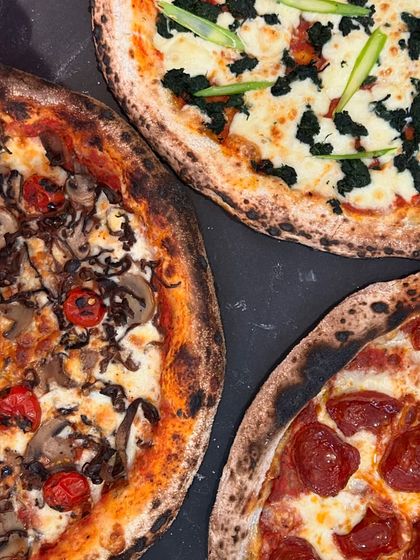 A beautiful trio of our wood-fired pizzas, showcasing the variety of toppings we offer. From pepperoni to veggie-loaded options, there's a pie for every palate.