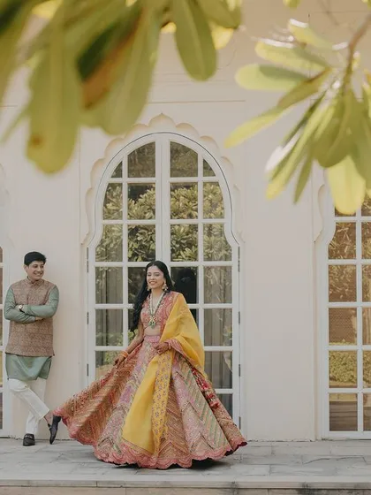 A wide shot capturing the couple against the beautiful architecture of The Oberoi Sukhvilas. The bride's twirling lehenga adds a sense of movement and joy to this Mehendi portrait.