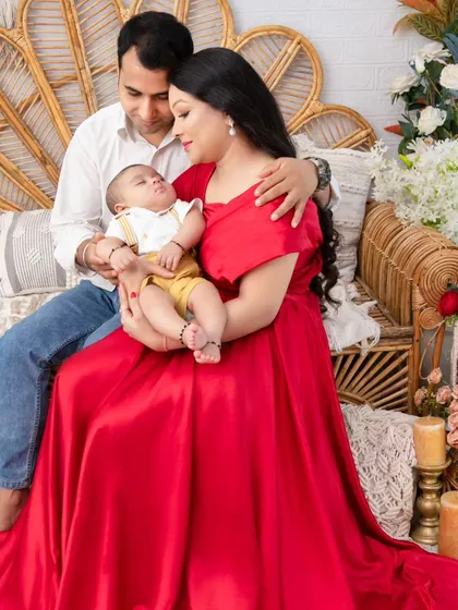 A quiet moment of adoration. In a vibrant red gown, the mother cradles her newborn, a classic portrait of maternal love set against our versatile boho backdrop.