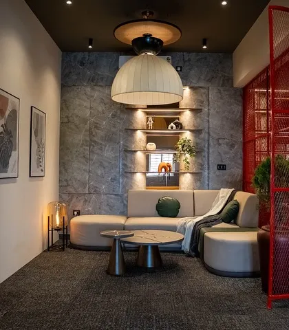 This informal meeting area is separated by a red mesh screen, adding a pop of industrial color while defining the space. The design combines a comfortable lounge setting with functional workspace elements.