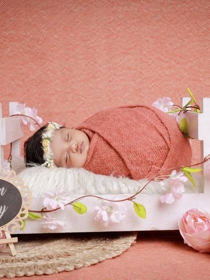 A 'Dream Baby' setup with a newborn sleeping on a miniature white bed adorned with pink flowers. This creates a soft, romantic, and dreamy scene.