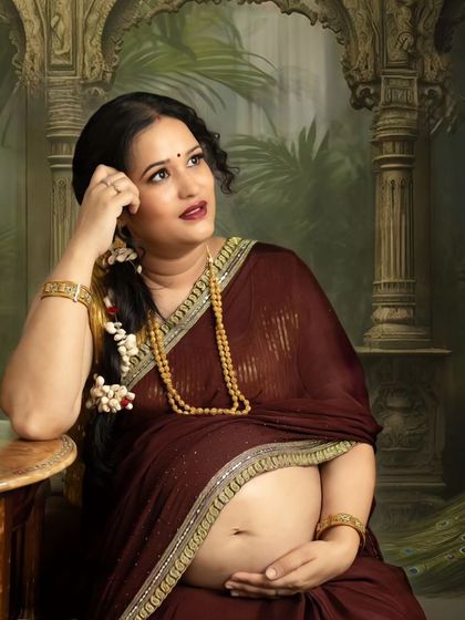 A thoughtful, seated portrait of a mom-to-be in a traditional saree, set against an ornate, palace-themed backdrop. This style of Indian maternity photography creates a regal and timeless feel.