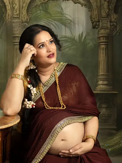 A thoughtful, seated portrait of a mom-to-be in a traditional saree, set against an ornate, palace-themed backdrop. This style of Indian maternity photography creates a regal and timeless feel.