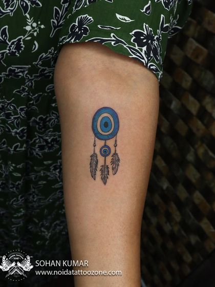 A small and colorful dream catcher tattoo. The bright blue of the evil eye charm makes this a protective and beautiful piece of minimalist body art.
