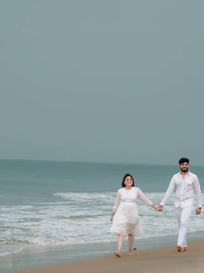 A beautiful wide shot of a couple walking hand-in-hand on a serene beach, capturing the vastness of the ocean and the sky.