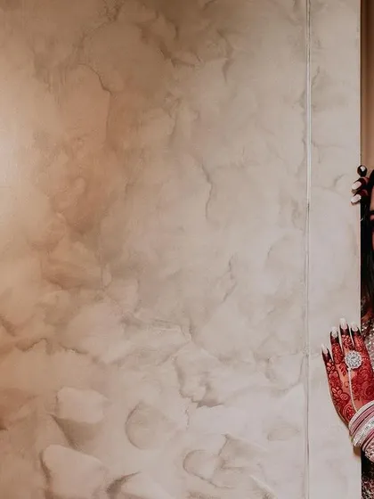 A portrait of a Muslim bride in a stunningly embellished gown, peeking from behind a wall.