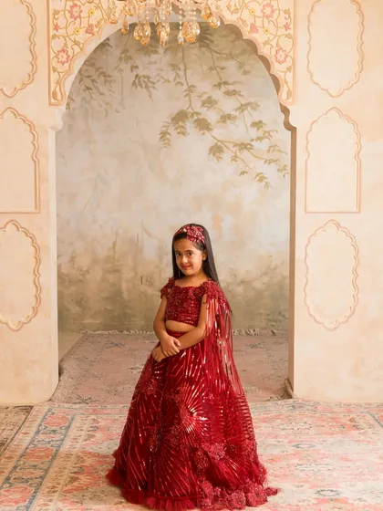 A classic red lehenga is a must have for any festive wardrobe. This custom stitched piece features shimmering sequin work and a delicate cape, ensuring she stands out at any wedding or celebration. We can customize this design in any color you choose.