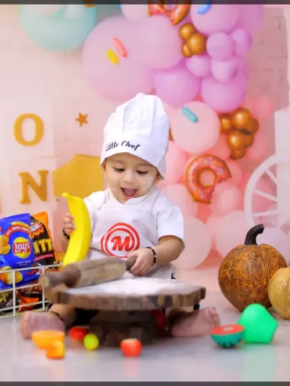 A happy 'Little Chef' enjoying his first birthday setup. The colorful balloon background adds a festive touch to this creative milestone session.